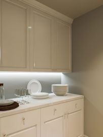 Cream-colored kitchen cabinets and countertop with stacked dishes, bowls, and glasses under under-cabinet lighting