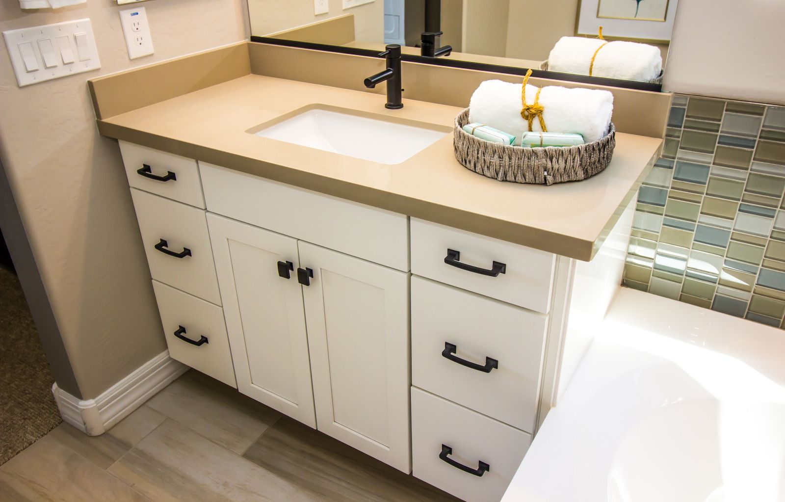 White bathroom vanity with sink, mirror, drawers, and woven storage basket on a light countertop.