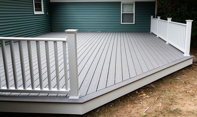 White-railed gray deck attached to a green house, viewed from the corner.