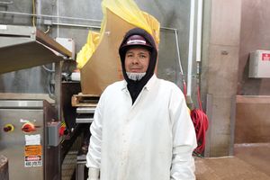 Person in a white coat and hard hat standing in an industrial kitchen, smiling at the camera.