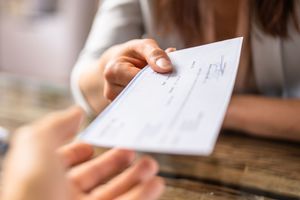 Handing over a white check at a table, with a hand reaching to receive it