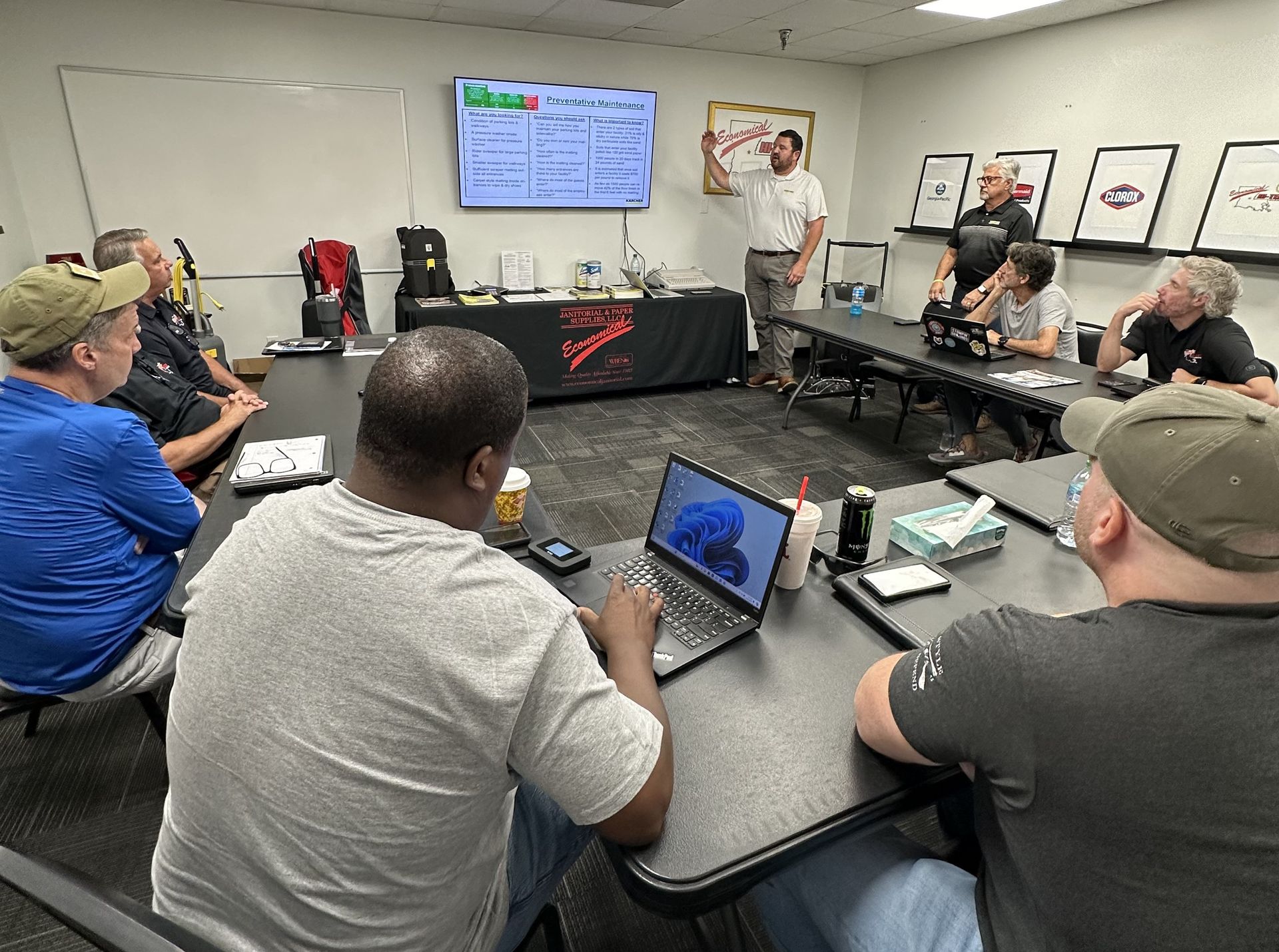 A group of men are sitting around a table with laptops in a room. A group of men are sitting around a table with laptops in a room.