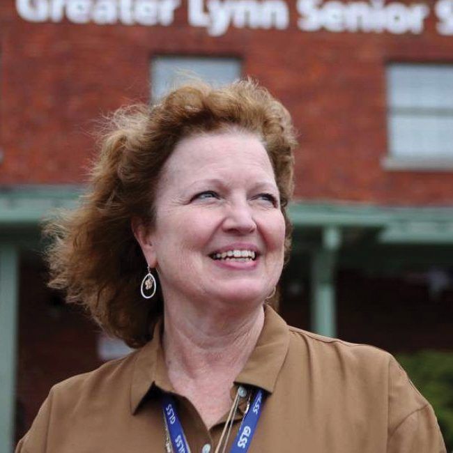 Woman smiles broadly, standing outside a brick building with