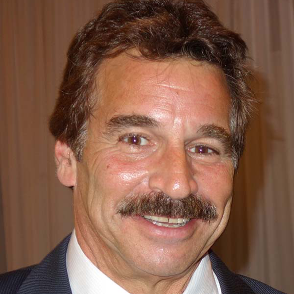 Man with a mustache smiles, wearing a suit.