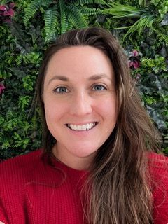 Smiling woman in a red sweater in front of a leafy green wall