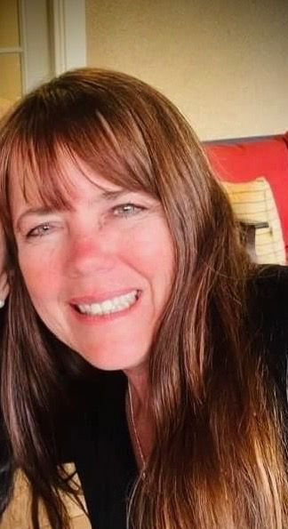 A woman with long brown hair is smiling for the camera while sitting on a couch.