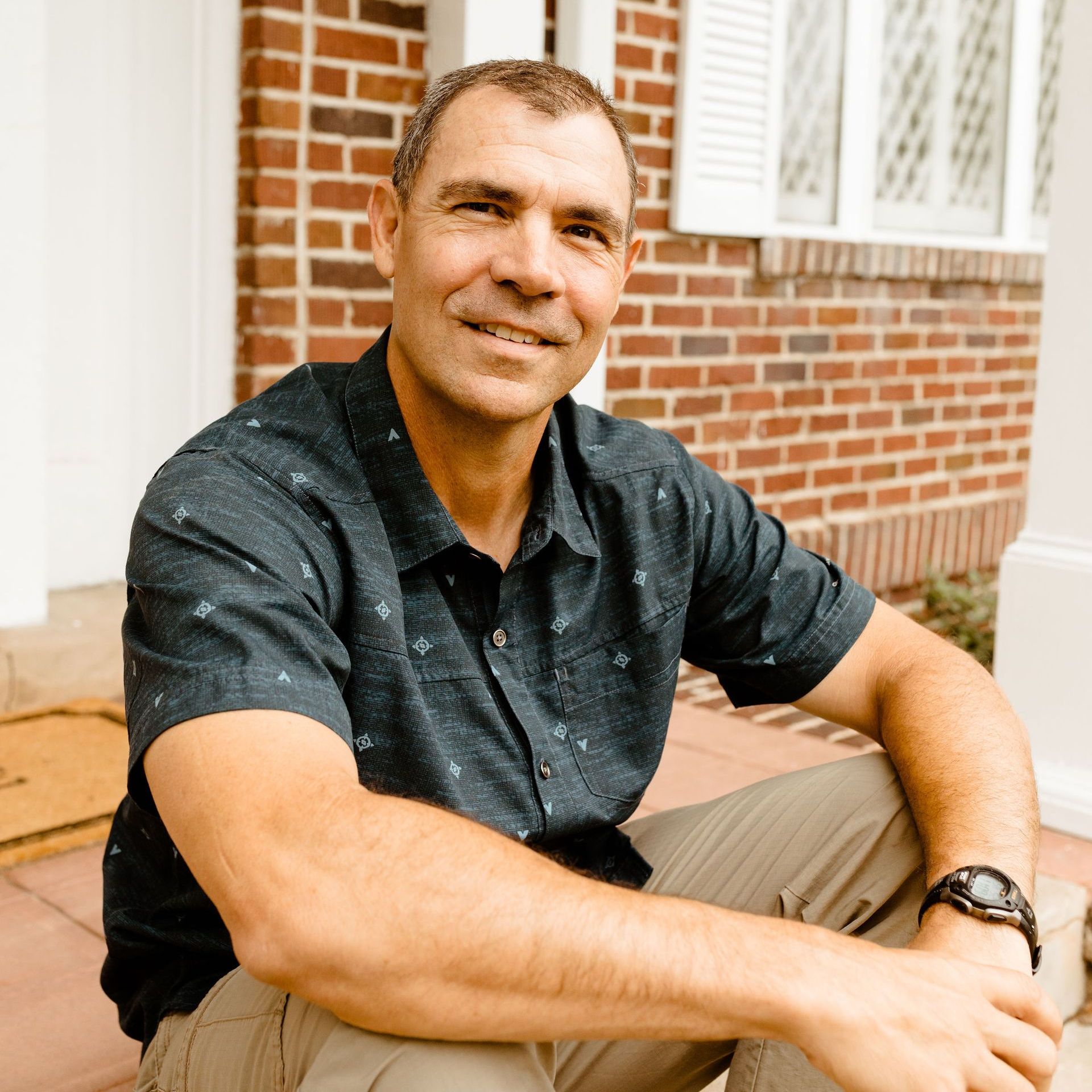 A man wearing a watch is sitting in front of a brick building