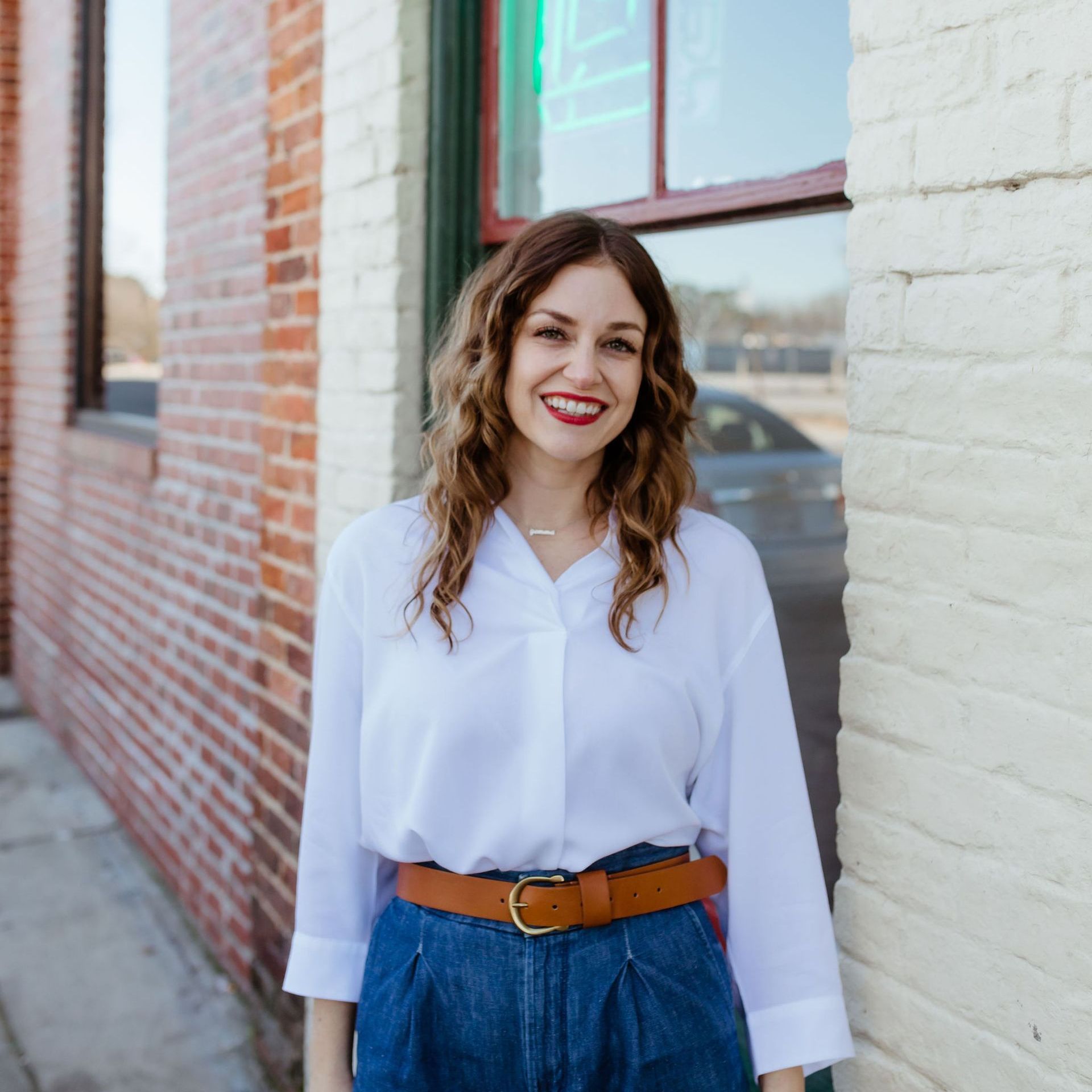 A woman wearing a white shirt and denim shorts is standing in front of a brick building.