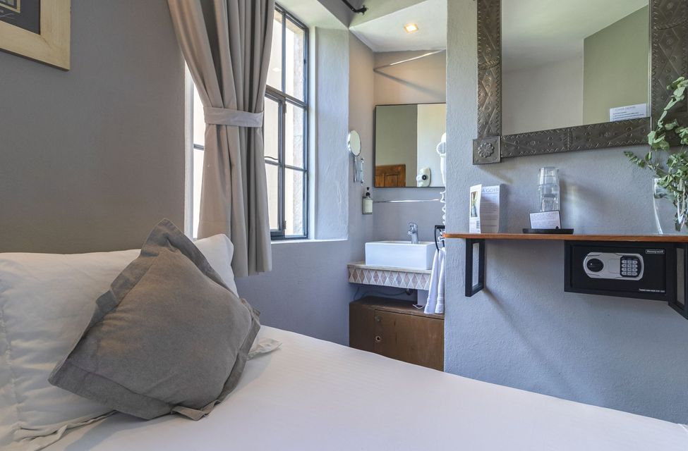 A hotel room with a bed , sink , mirror and safe.