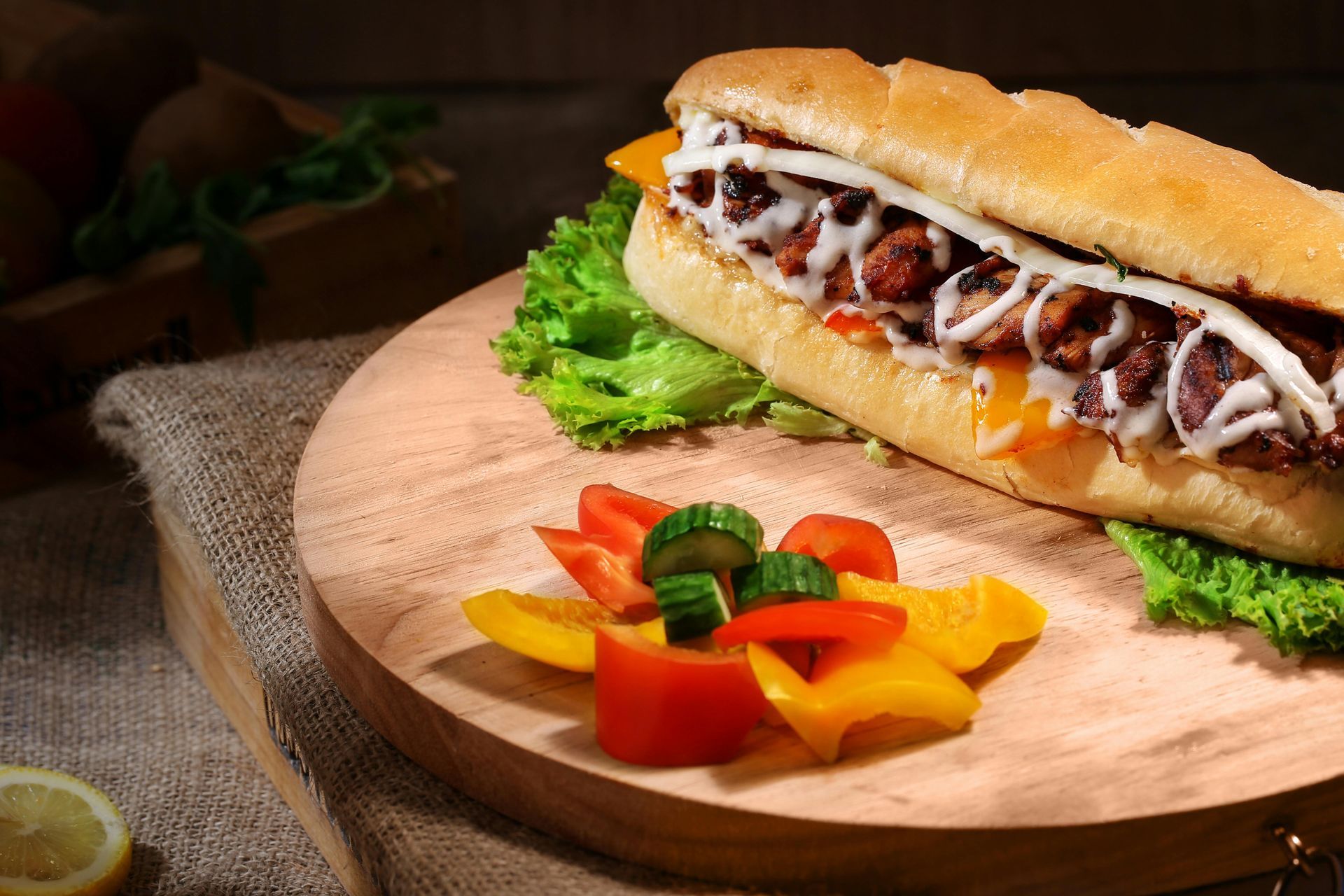 Sandwich on a wooden board with lettuce, tomatoes, peppers, and jalapeños
