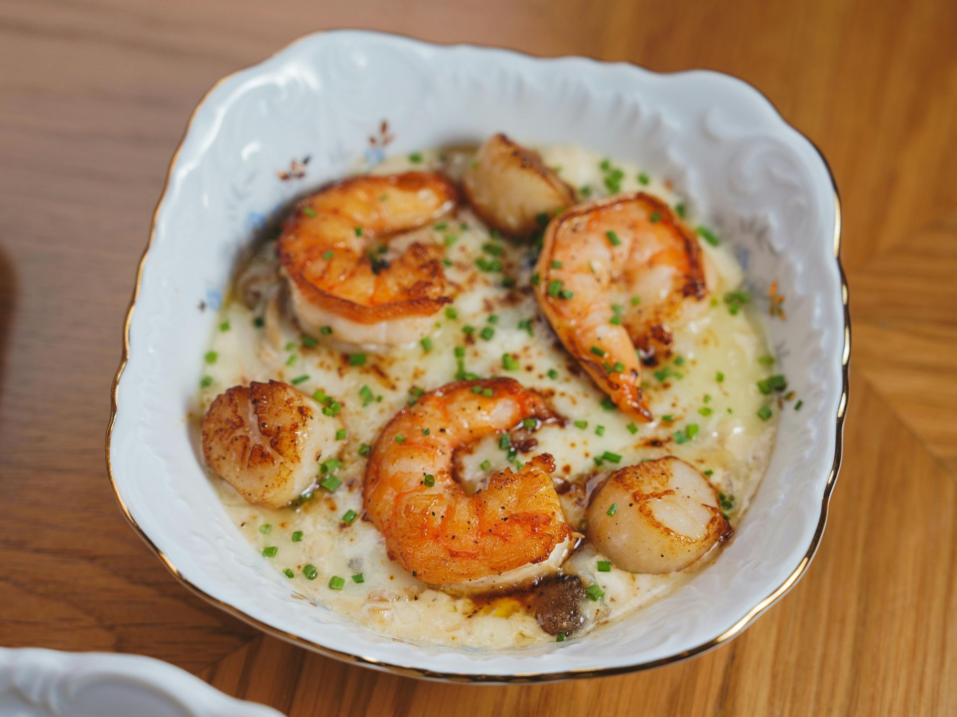 Baked scallops in a creamy sauce, garnished with herbs, in a white scalloped dish