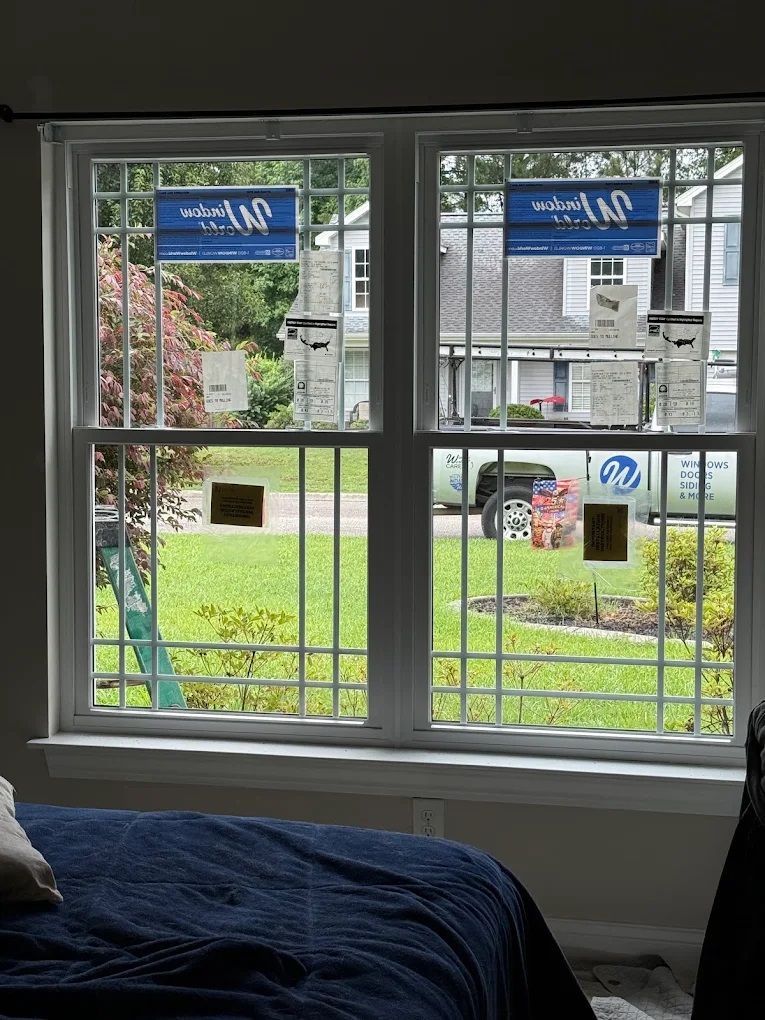 Bedroom window with white grid panes overlooking a grassy yard and neighboring houses.