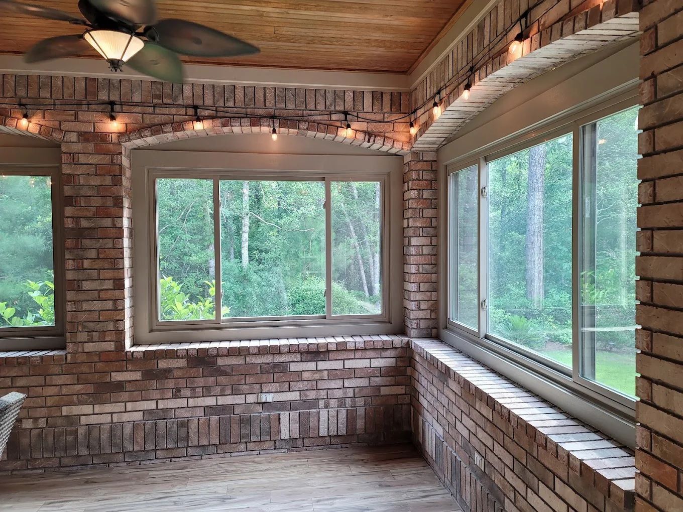 Brick sunroom with large windows, wood ceiling, and views of green trees outside
