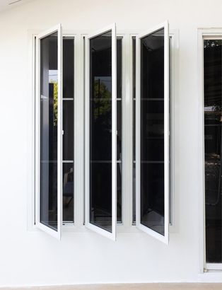 White wall with three narrow open casement windows and a partially visible window on the right