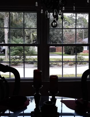 Dining room table by a window overlooking a garden, with hanging lights and silhouetted chairs indoors.