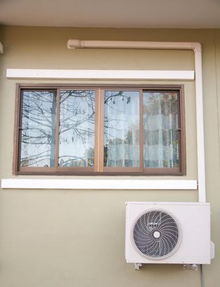 Window with brown frame on beige wall, white trim, and a wall-mounted air conditioner below