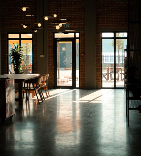 Sunlit café interior with brick walls, hanging lights, tables, and large windows overlooking a balcony