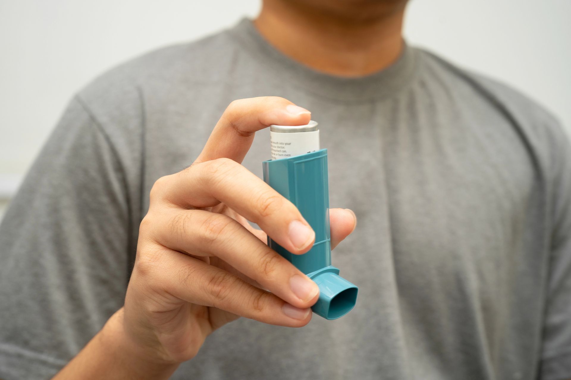 Una persona con una maglietta grigia che tiene in mano un inalatore predosato blu.