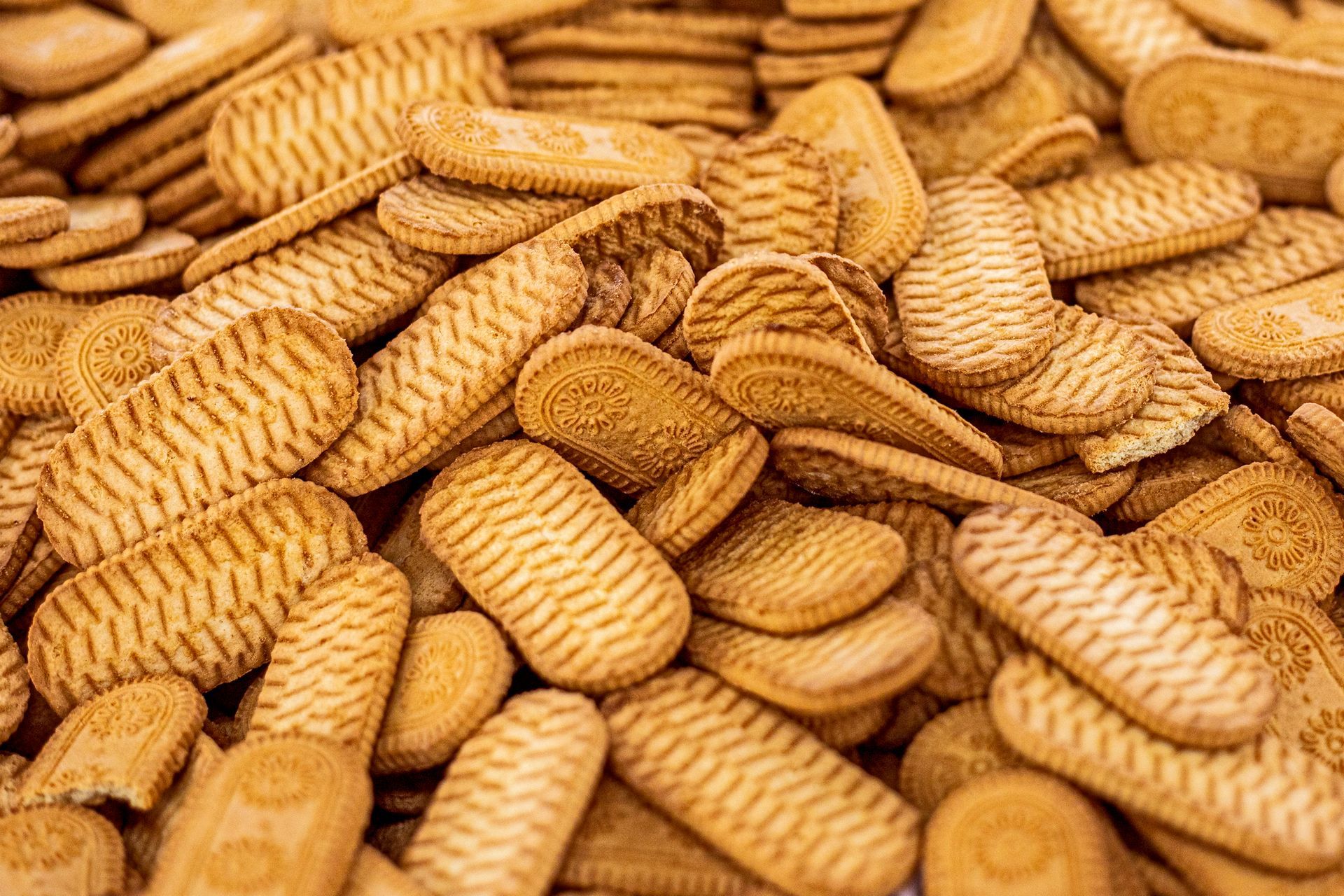 Un grande mucchio di biscotti rettangolari color marrone dorato con superficie ruvida e scanalata.