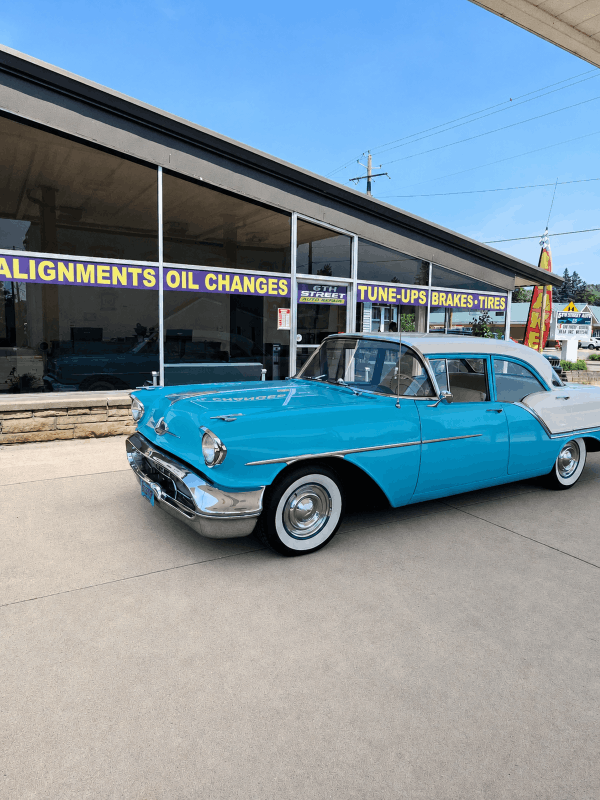 Bright blue vintage car parked outside the 6th Street Auto Repair shop under a clear sky