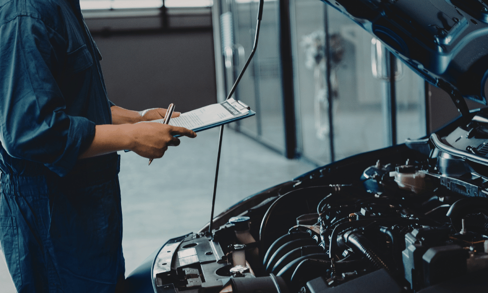 Technician performing vehicle inspection with checklist under hood