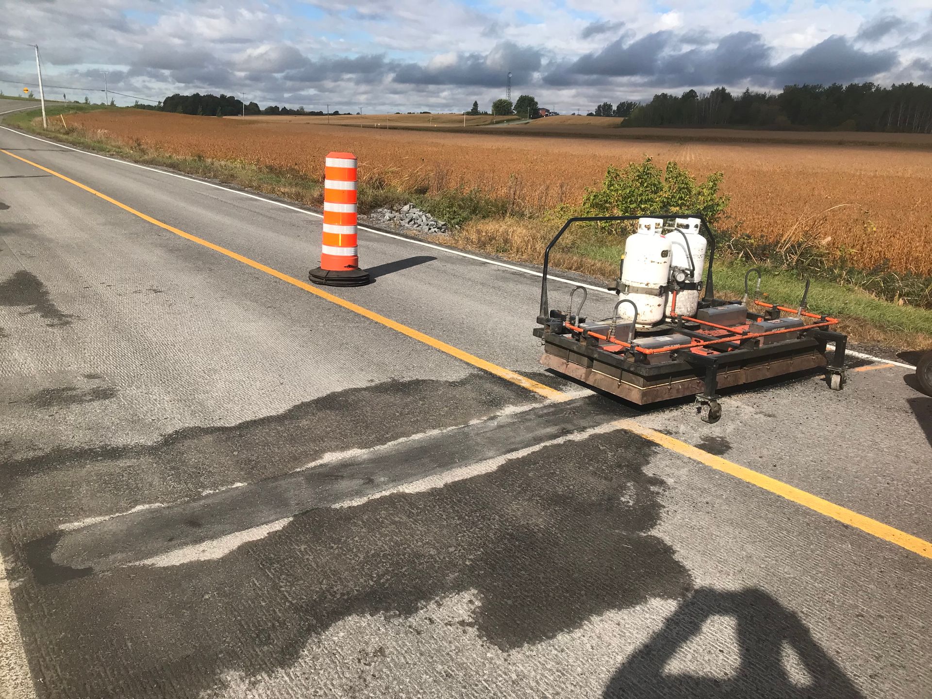 Matériel de réparation routière avec cône orange en bordure d'une route rurale, près d'un champ