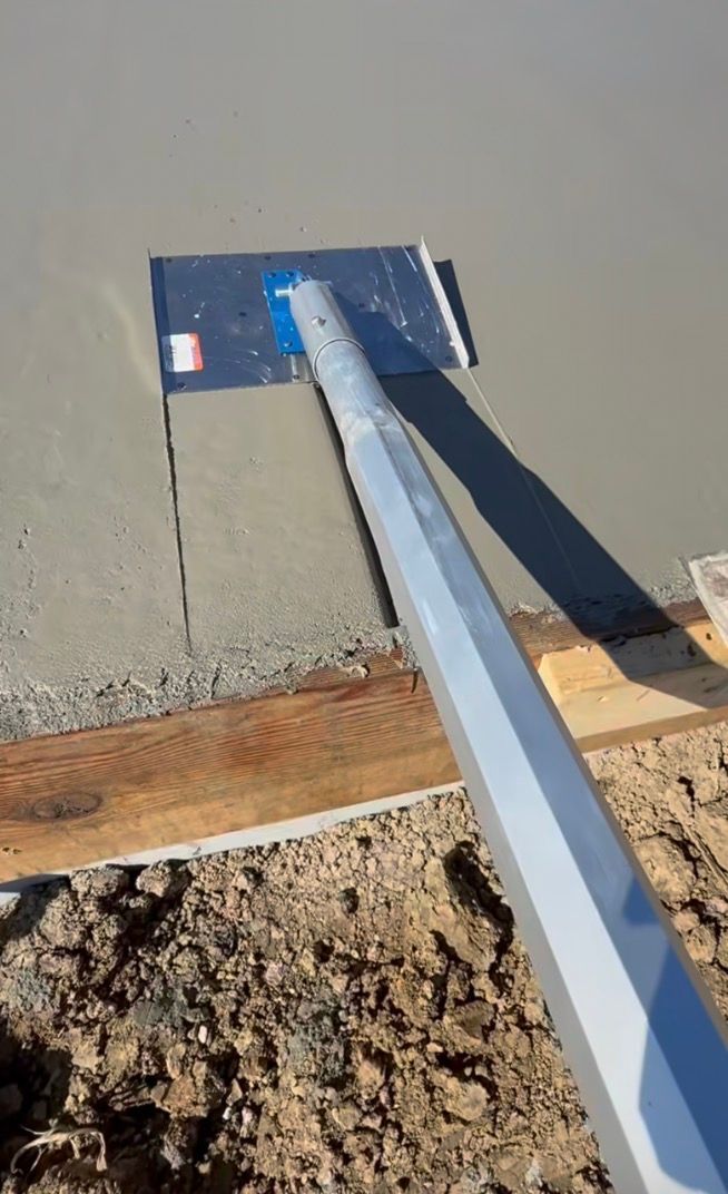 Raclette à long manche lissant le béton frais le long d'un bord de terre boueuse