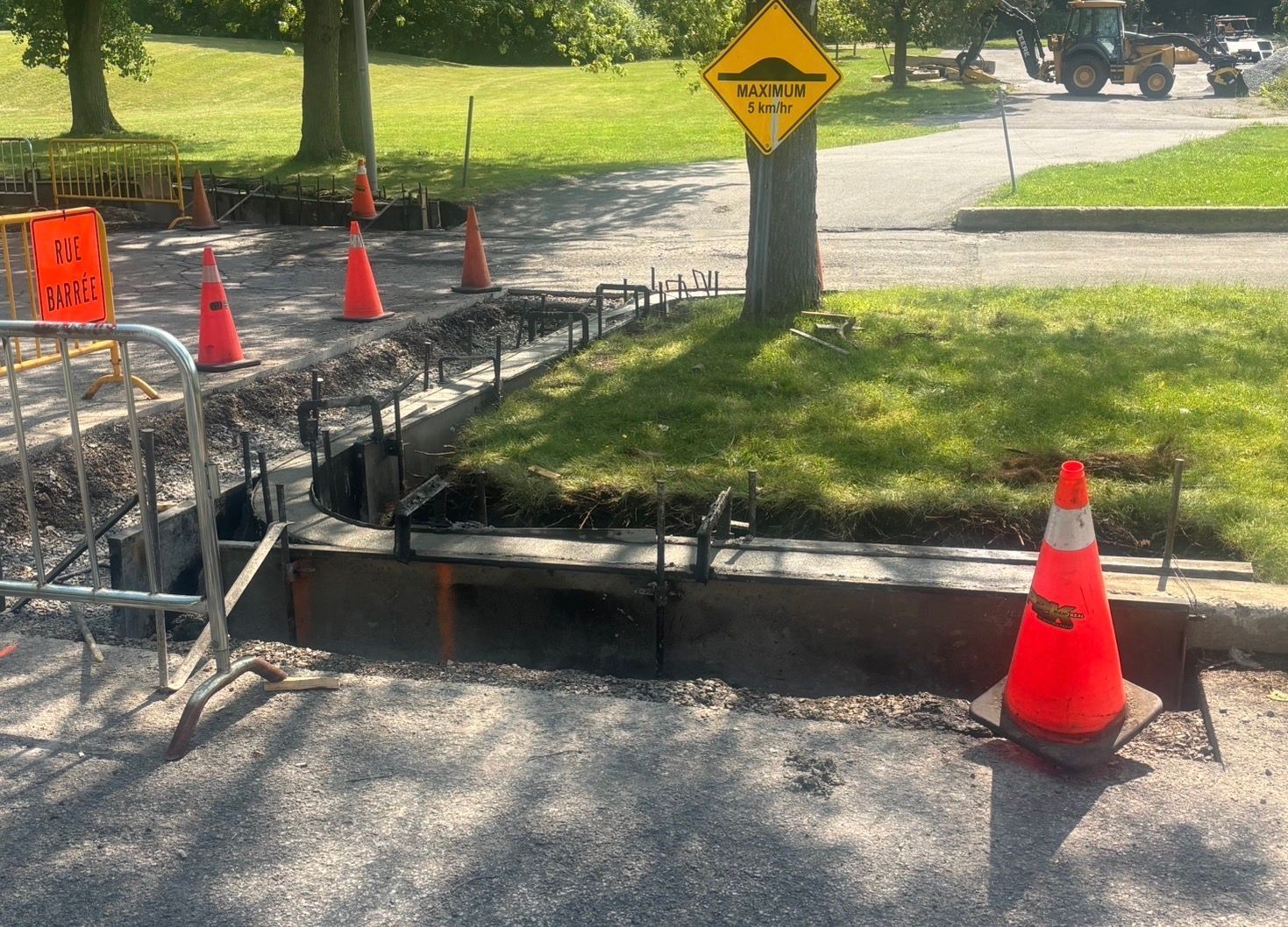 Tranchée technique en bordure de trottoir, signalée par des cônes orange et des panneaux de signalisation.