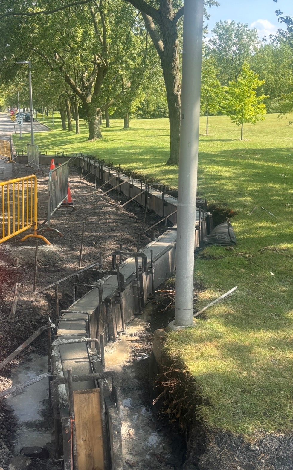 Tranchée de construction et coffrage en béton le long d'un sentier de parc bordé d'arbres et de pelouse