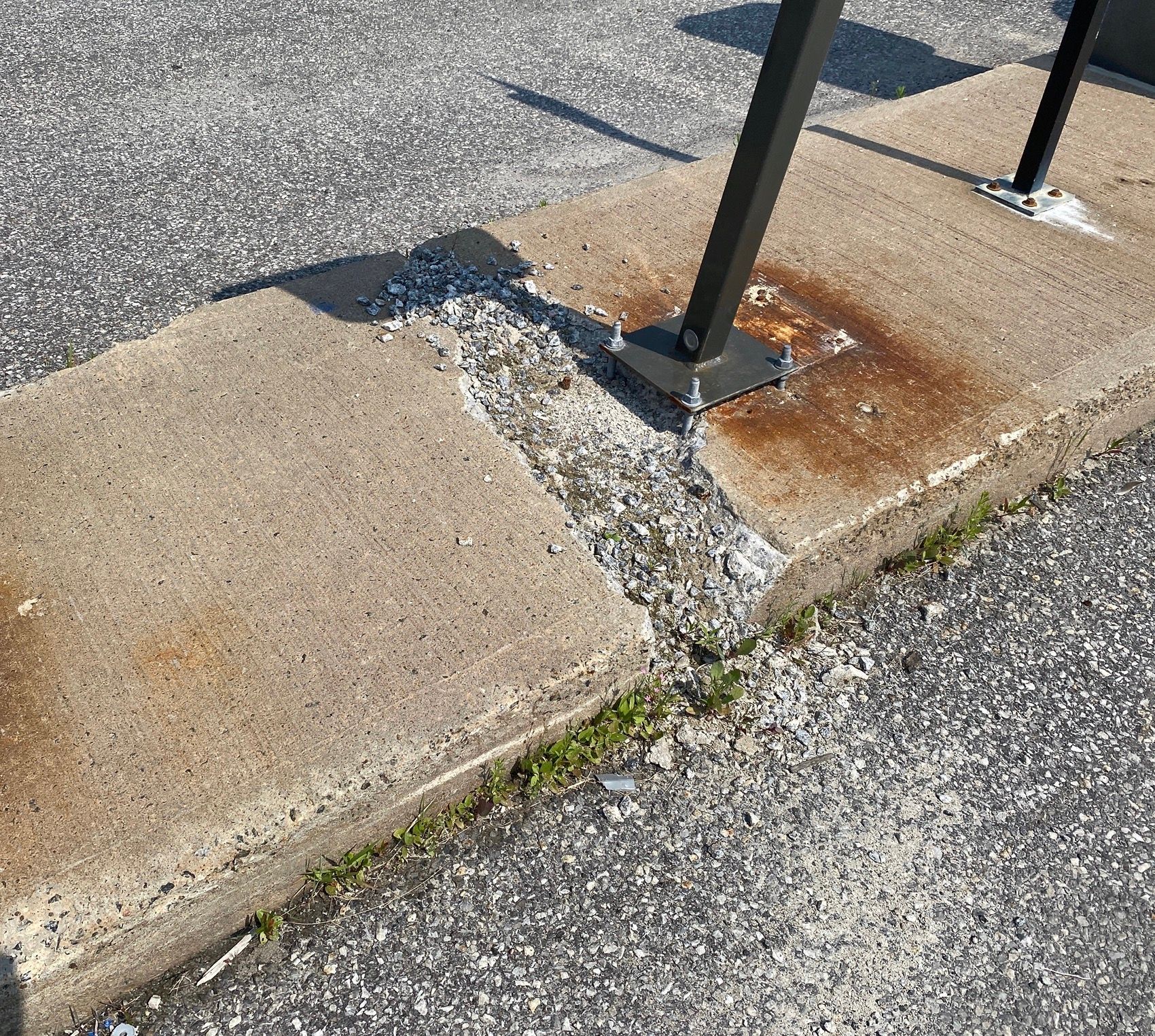Rampe d'accès endommagée avec béton fissuré et poteau métallique rouillé en bordure d'un parking