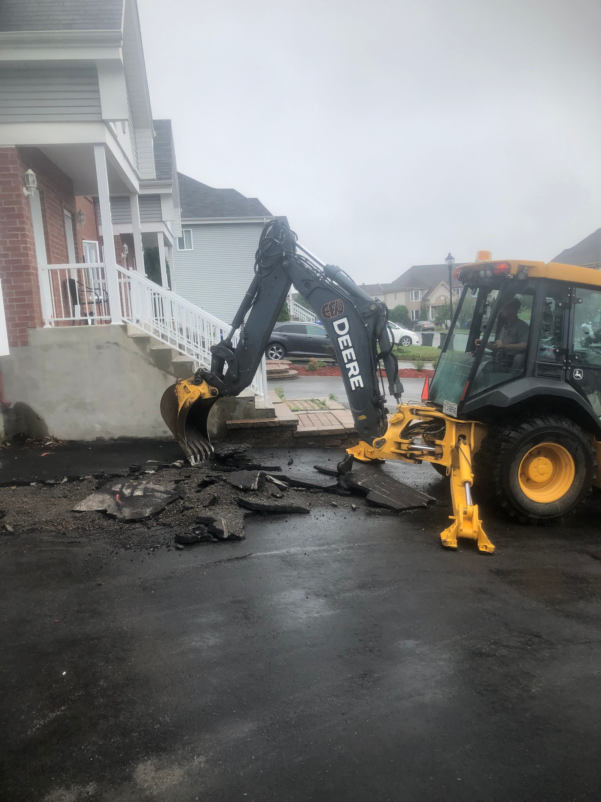 Une excavatrice jaune et noire creuse un trou dans le sol devant une maison.