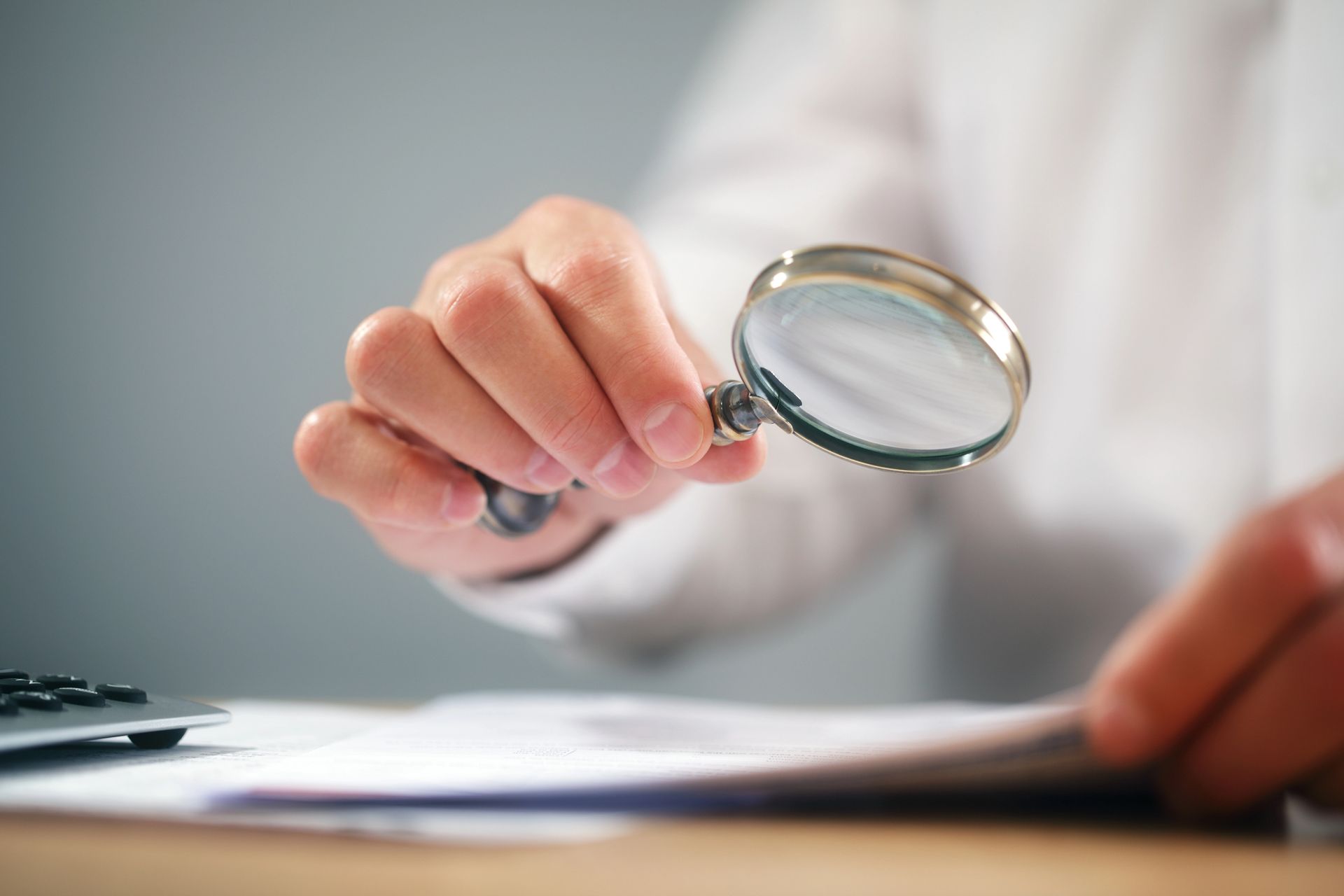 Una mano sostiene una lupa sobre unos documentos en un escritorio.