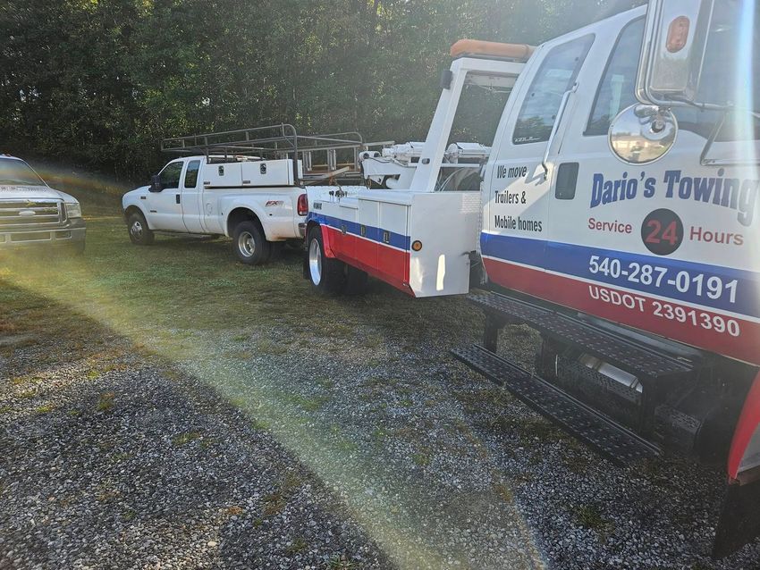 Tow truck towing a white pickup on a gravel roadside in the rain