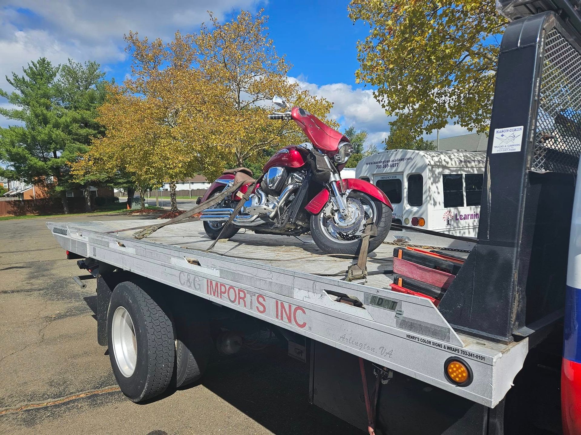 Red motorcycle secured on a flatbed tow truck in a parking lot, with autumn trees in the background