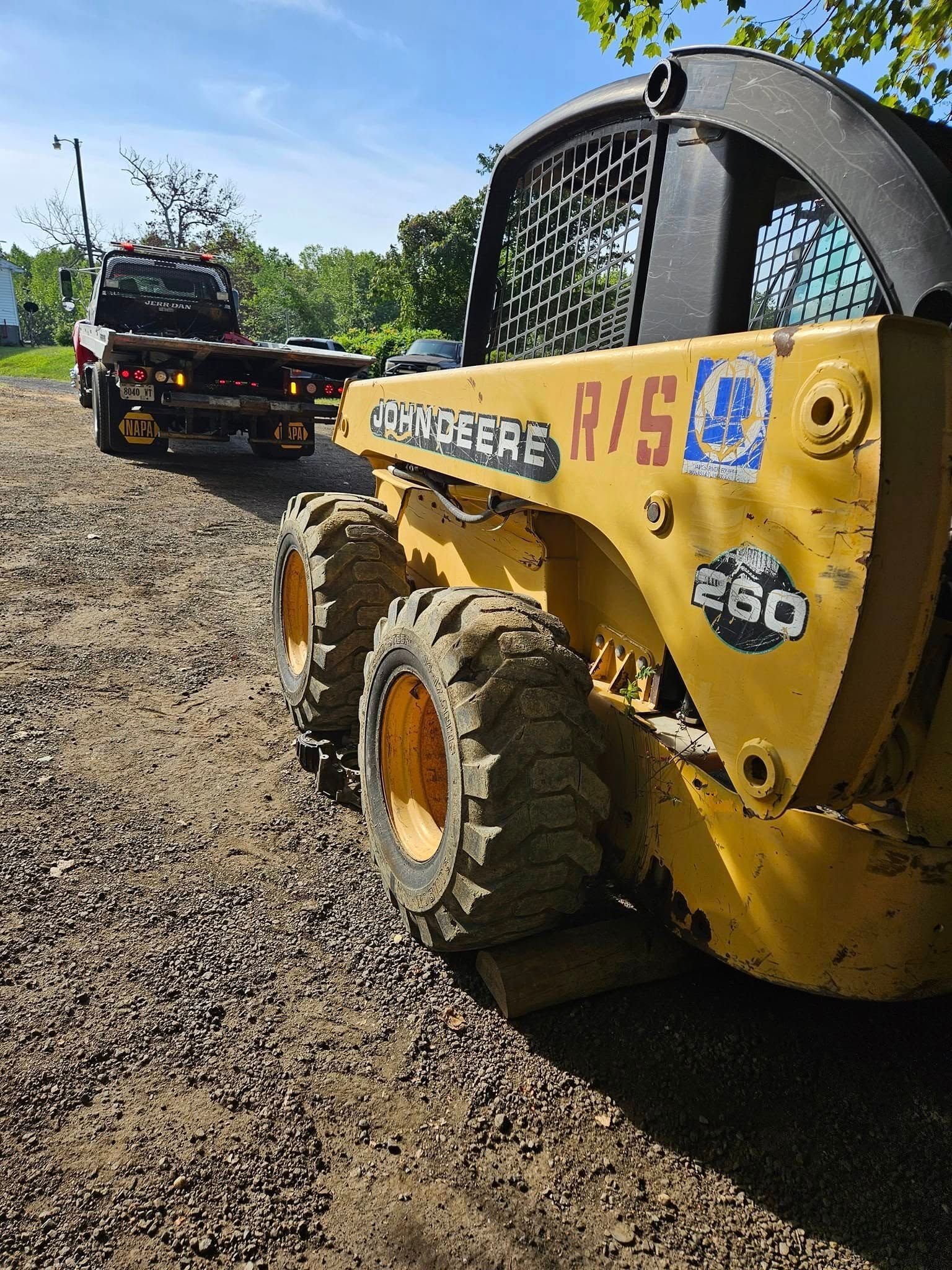Yellow road roller on a gravel road under a blue sky, with construction equipment in the background