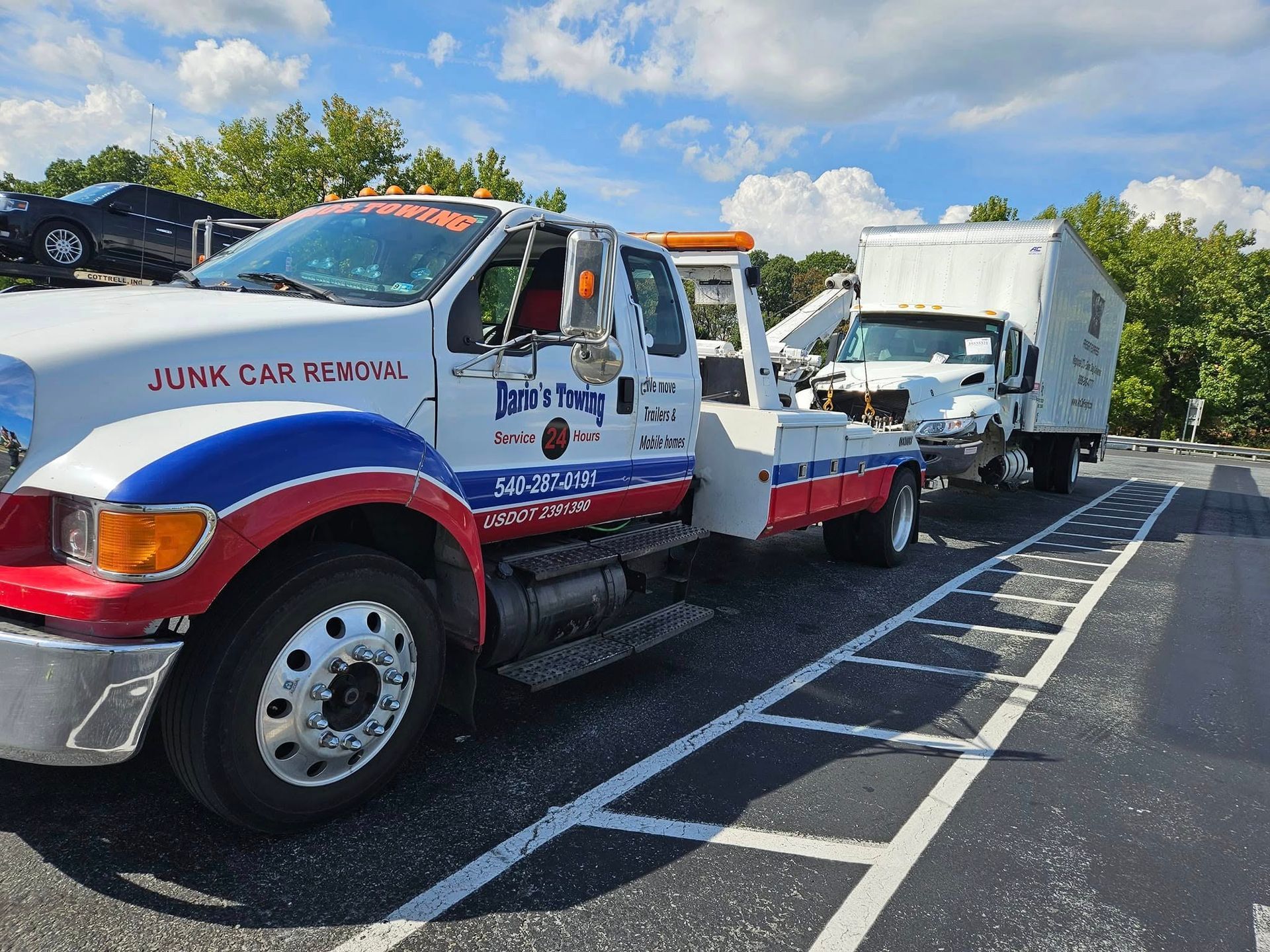 Tow truck hauling a white box truck on a sunny roadside parking lot