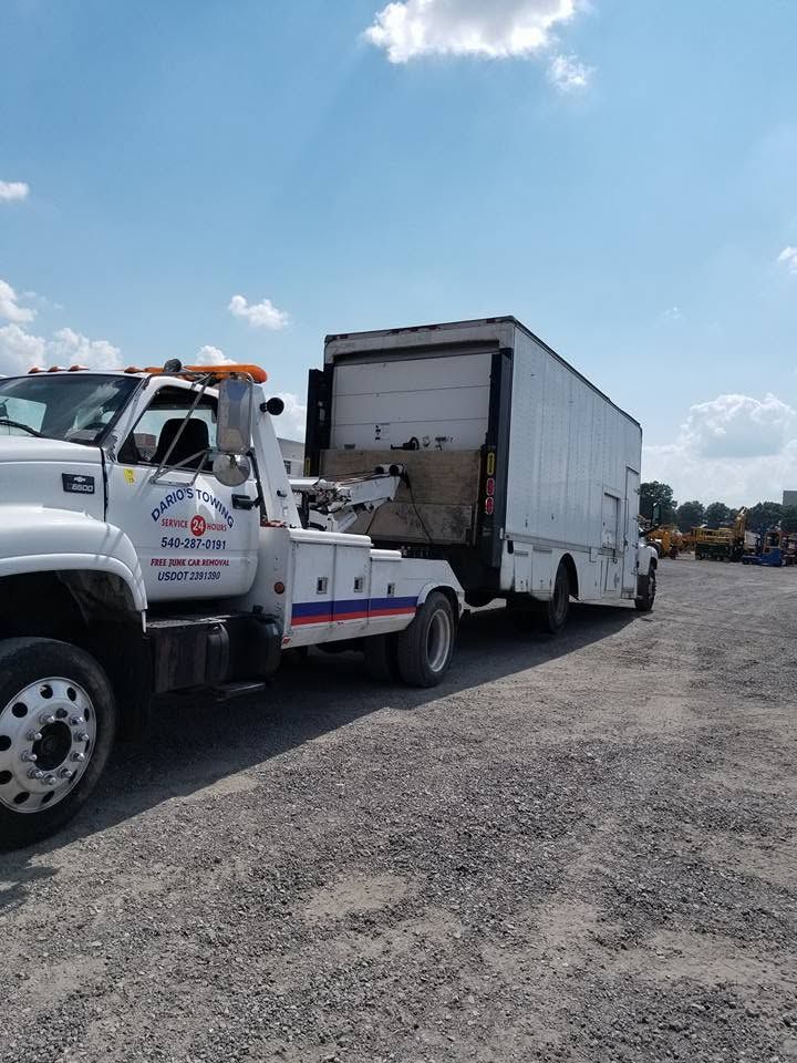 Tow truck hauling a white box truck in a gravel lot under a blue sky