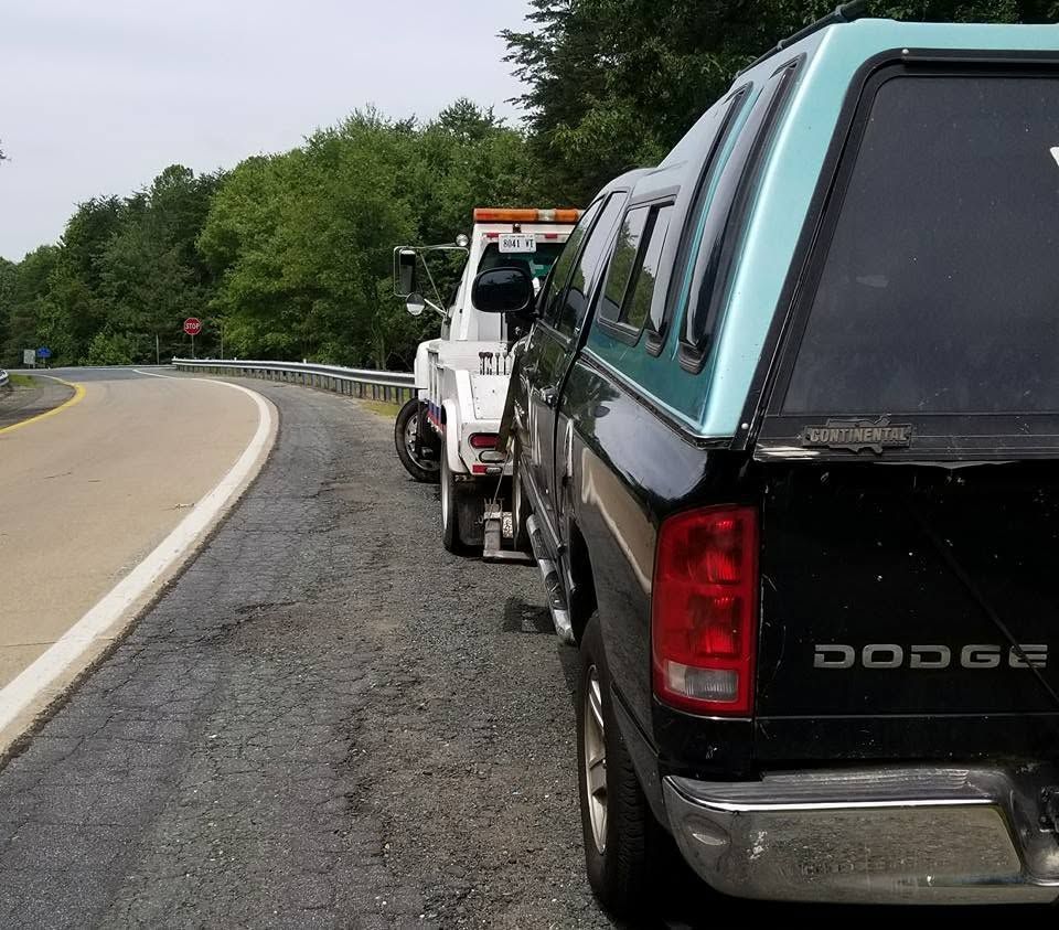 Tow truck hauling a teal Dodge pickup on a curved roadside shoulder