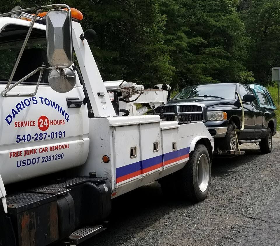 Tow truck hauling a black SUV on a gravel road with trees in the background