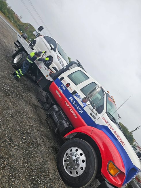Tow truck with blue, red, and white livery parked on a wet roadside under a gray sky