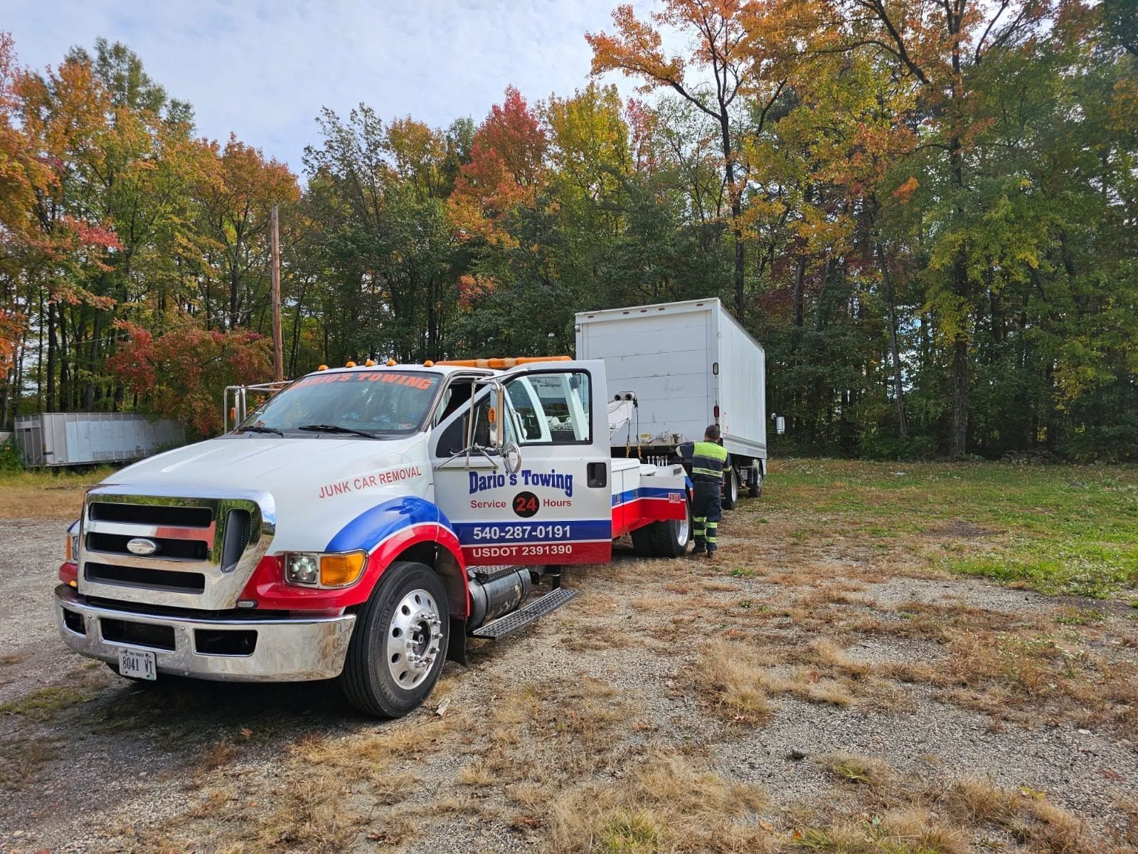 Two utility trucks parked on a dirt lot beside autumn trees