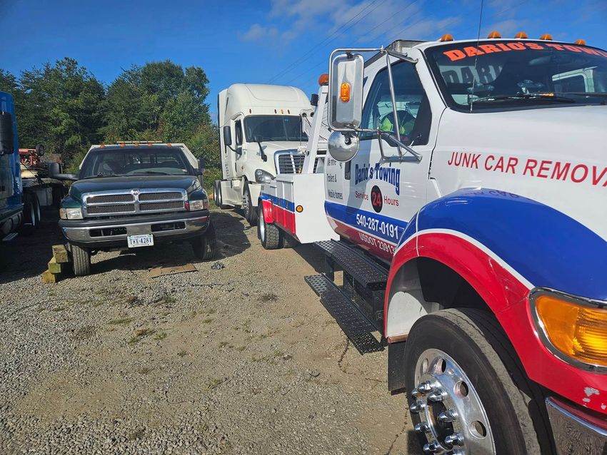 Tow truck and black pickup truck in a gravel lot under a blue sky