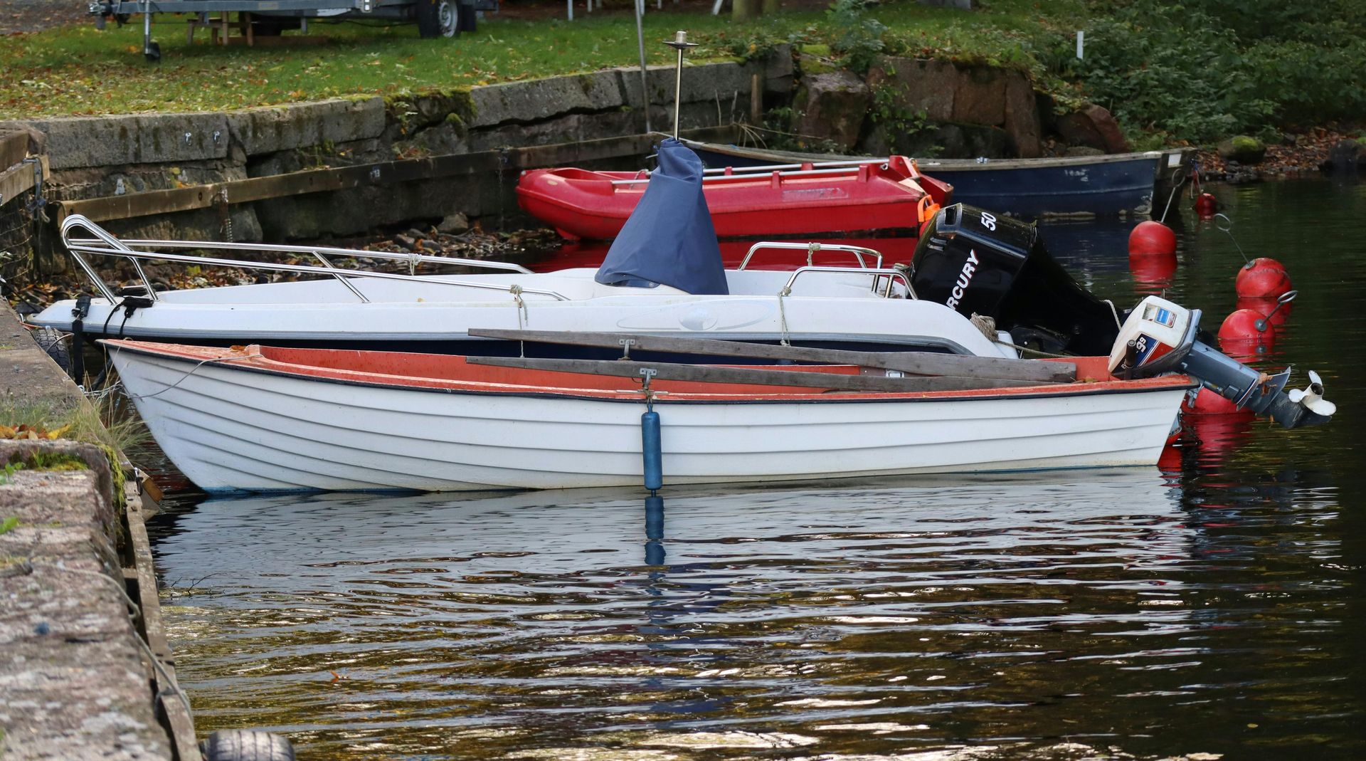 White boat with orange stripe moored on a calm river beside red buoys and a grassy bank