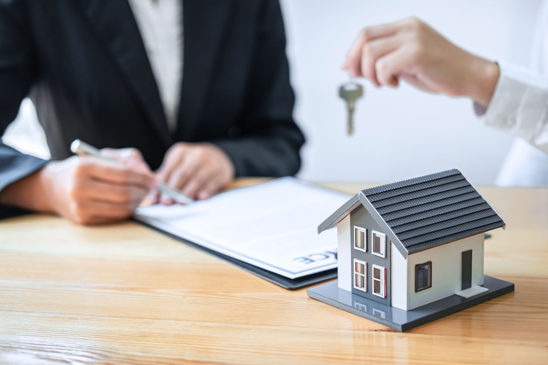 Businessperson signing paperwork beside a small model house on a desk