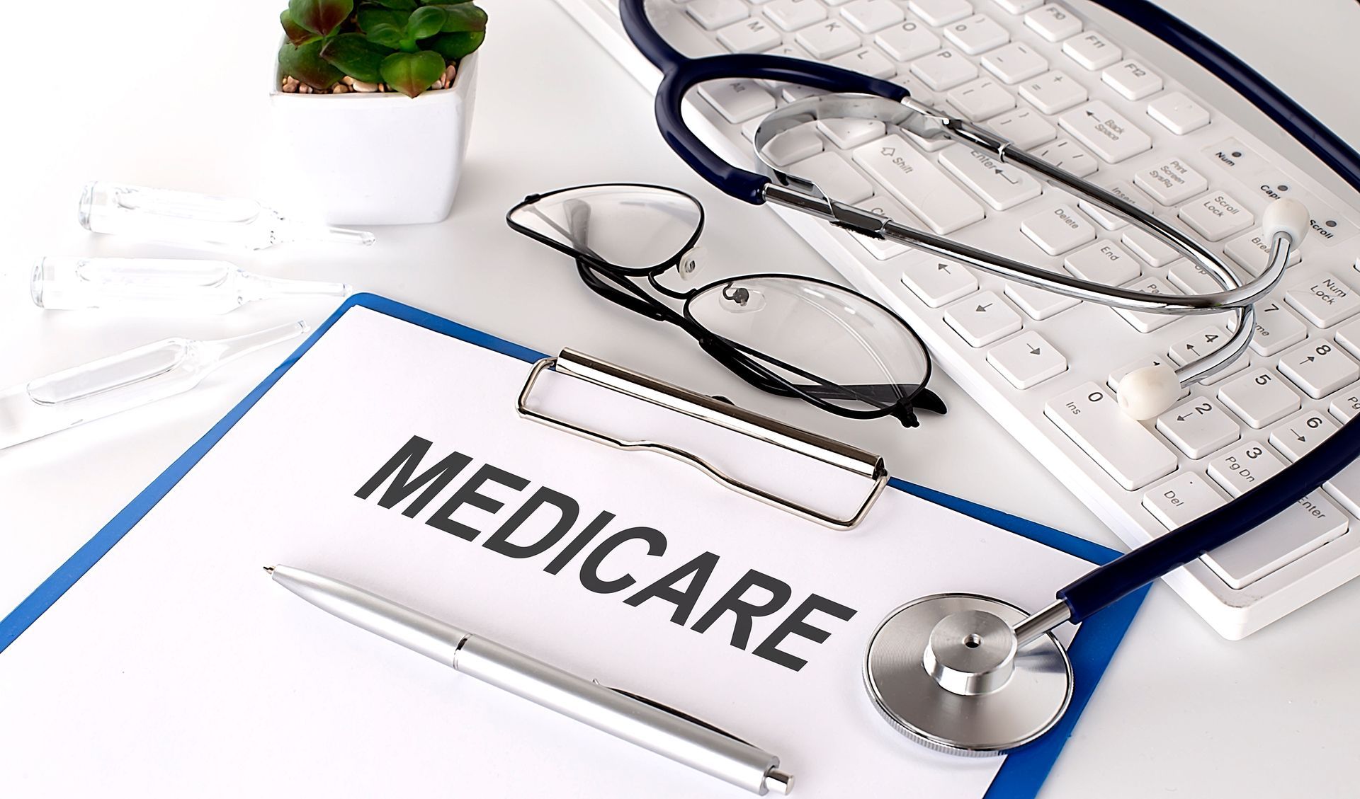 Medicare folder with stethoscope, eyeglasses, and keyboard on a white desk