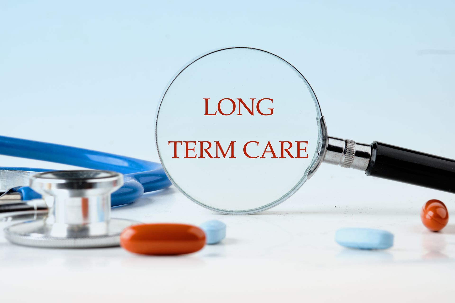 Magnifying glass over “LONG TERM CARE” on a desk with a stethoscope and pills