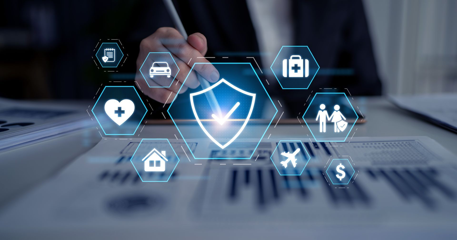 Hand selecting a glowing shield icon on a laptop, with health, car, home, and family icons around it
