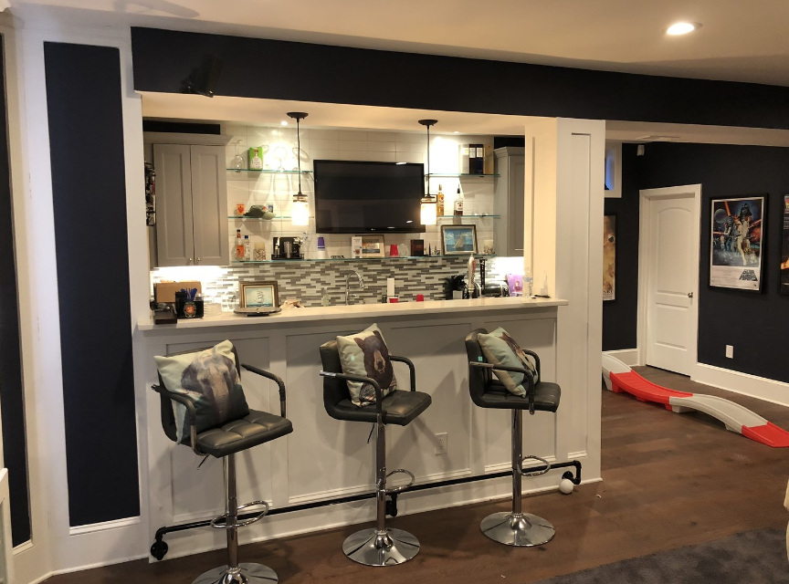 A basement bar with three stools and a television.