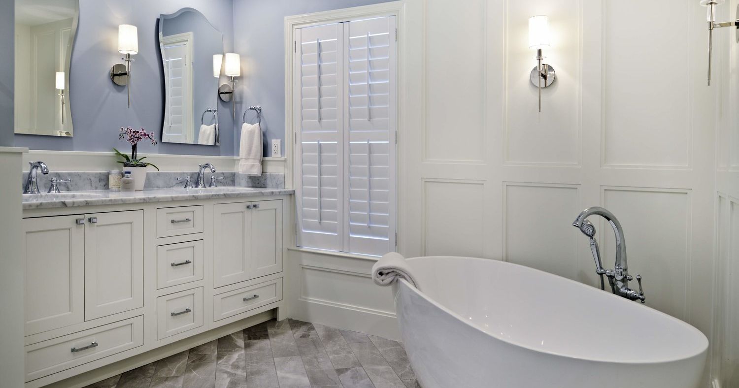 A bathroom with two sinks , a tub , and a mirror.