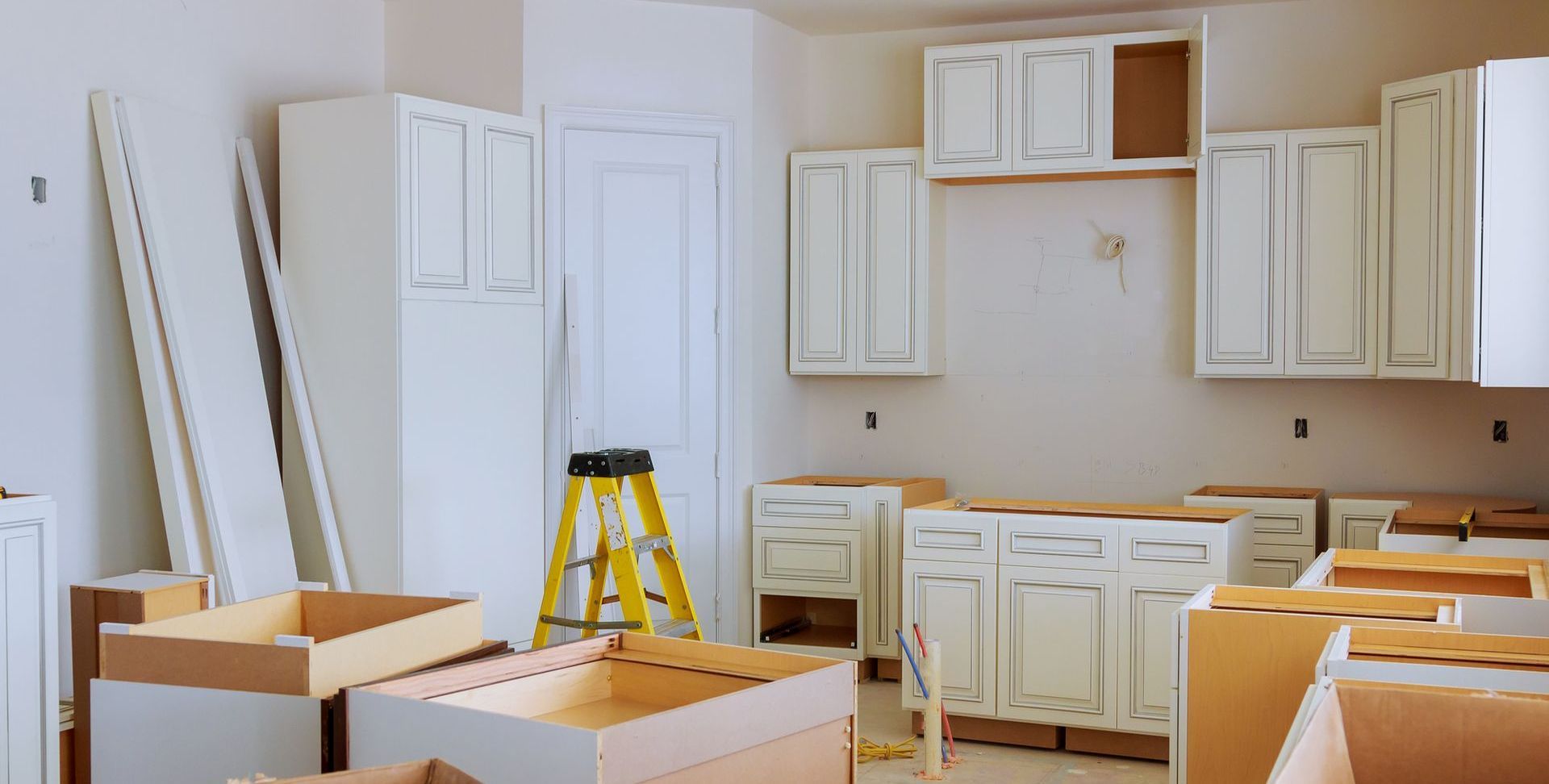 A kitchen is being remodeled with white cabinets and a yellow ladder.